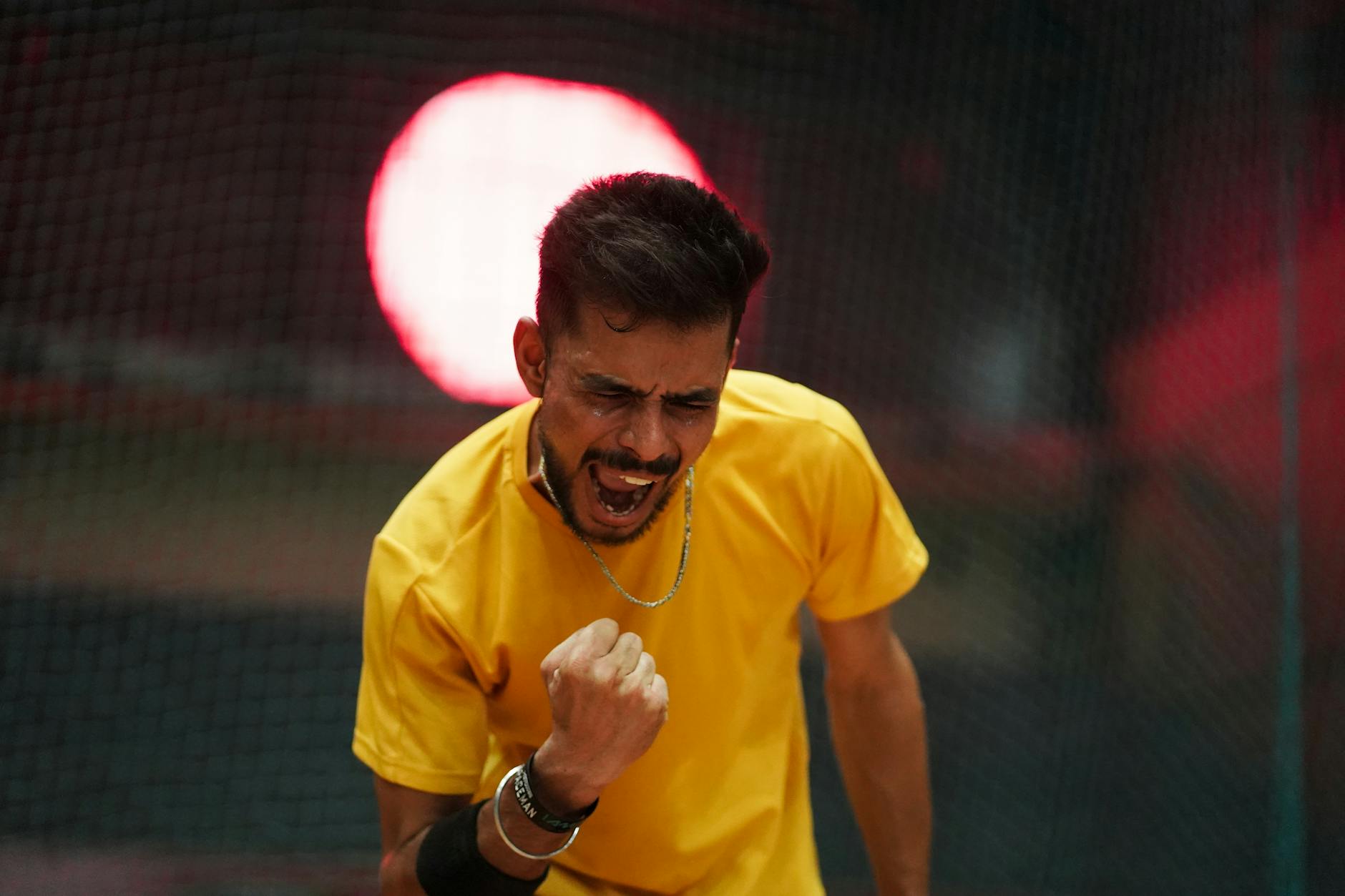 Man in yellow shirt celebrating a victory indoors with dramatic lighting.