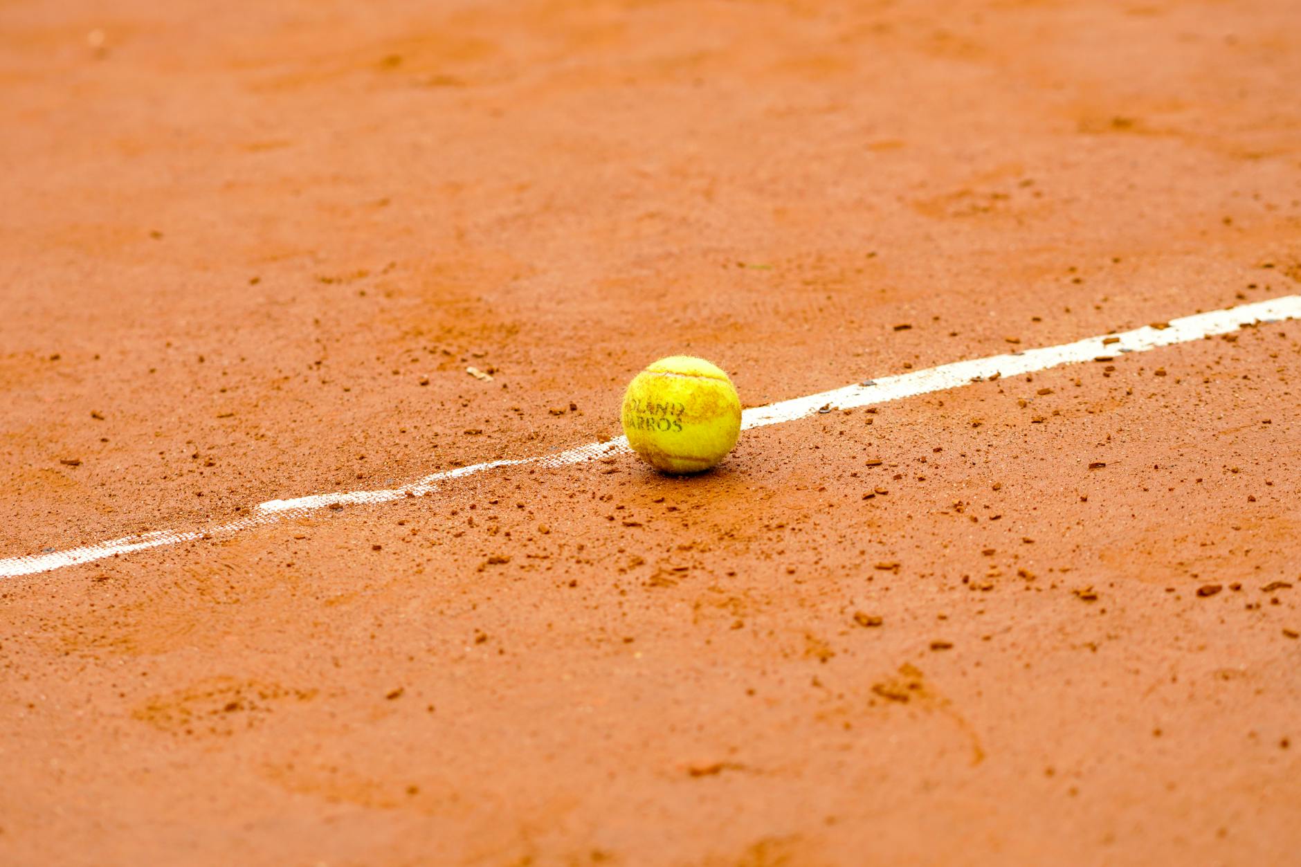 Tennis ball resting on a clay court, marked by a white line, ideal for sports themes.