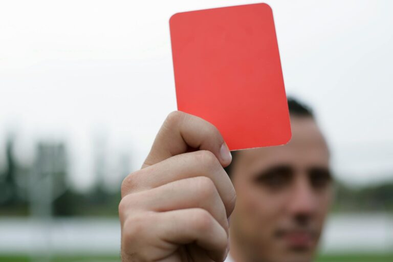 Close-up of a referee holding a red card, signaling a penalty in a soccer match.