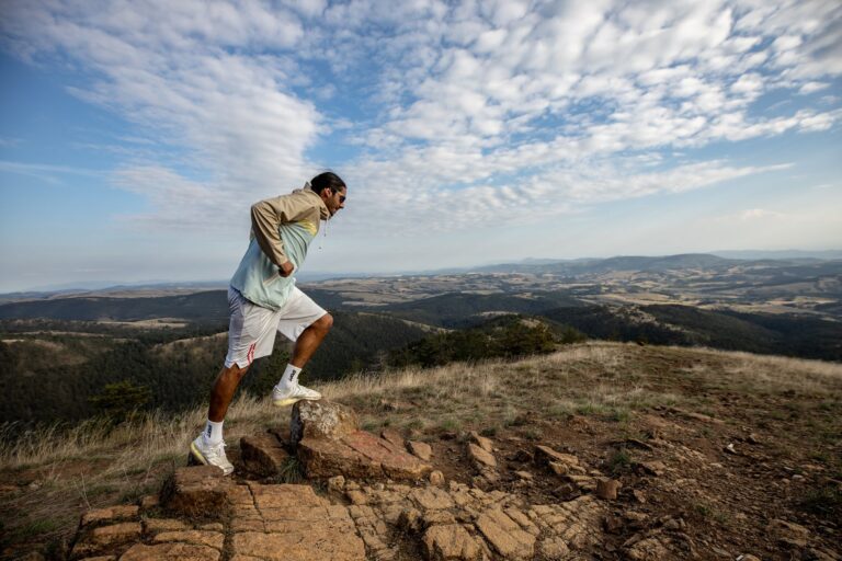 A man jogging on a scenic mountain trail, surrounded by vast landscapes under a clear sky.