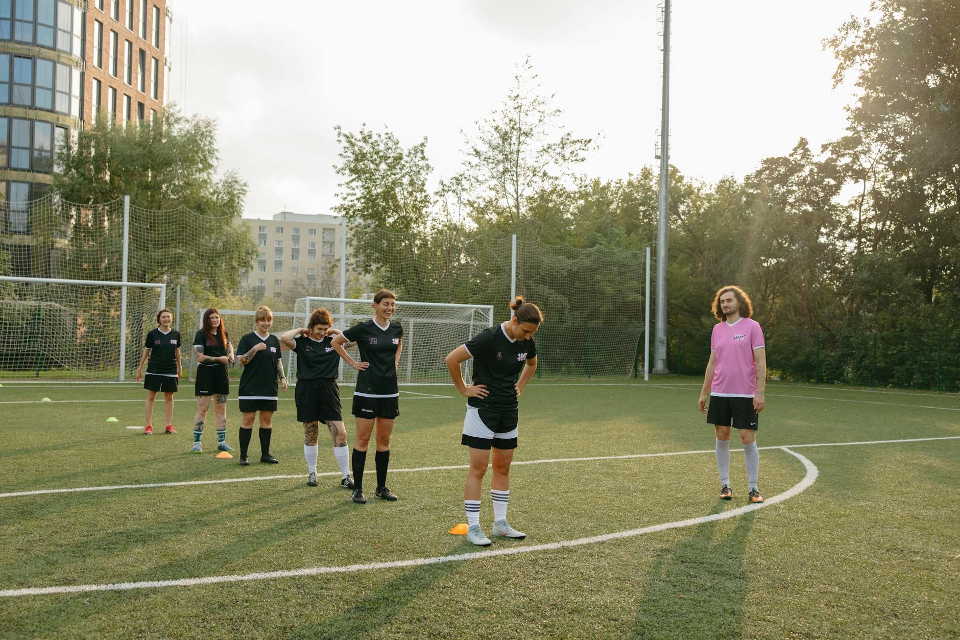 Women's soccer team practices drills on a sunny outdoor field with coach observing.