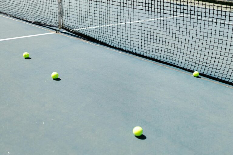 A tennis court featuring a net and several tennis balls lying on the ground, well-lit by sunlight.