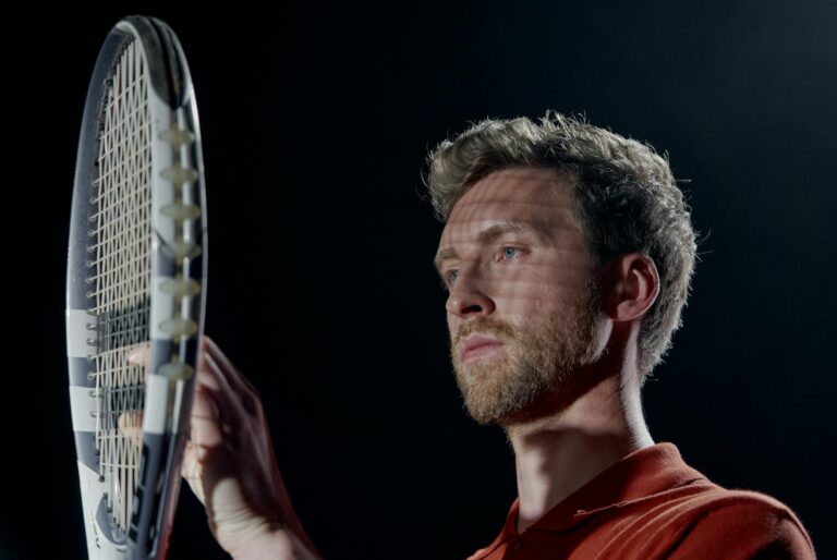 Portrait of a serious male tennis player holding a racket with a black background.