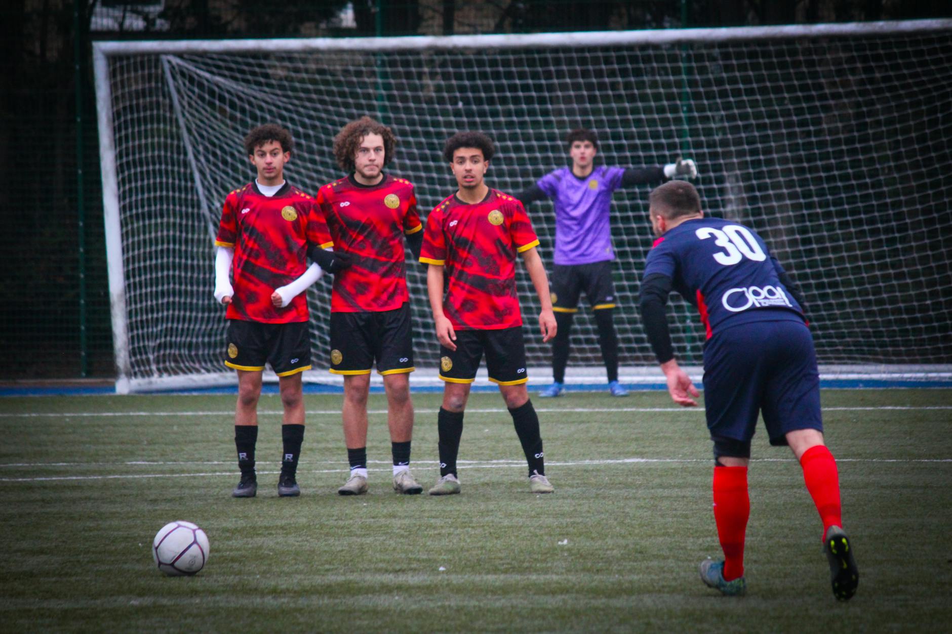 Soccer players setting up for a freekick on a grass field with goalkeeper ready.