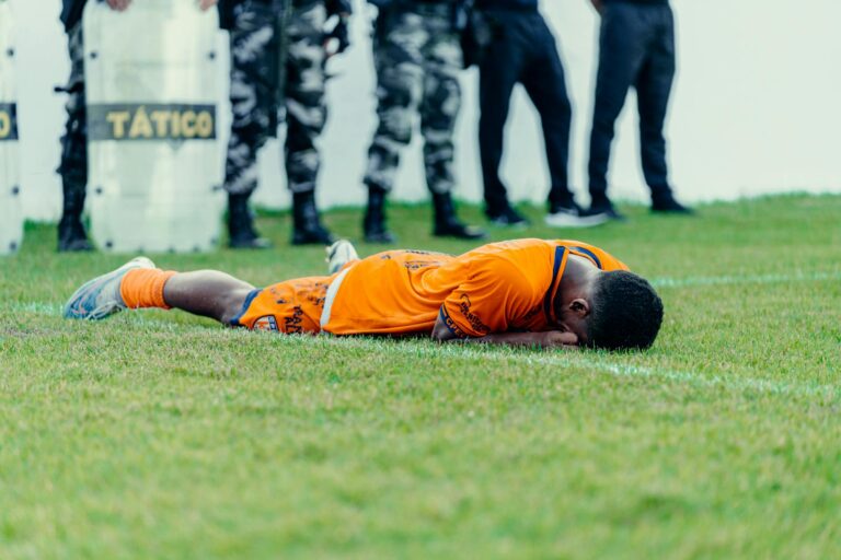 Injured football player in orange jersey lying on field with police presence.