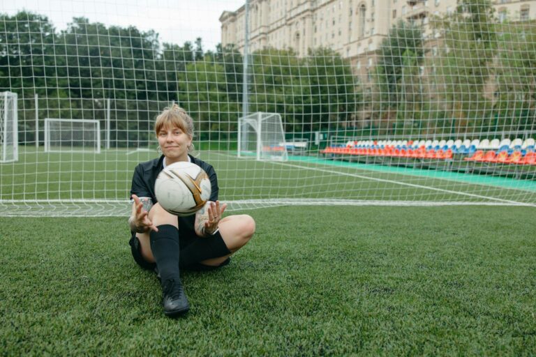 A female soccer player sitting with a ball on a soccer field, enjoying a break.