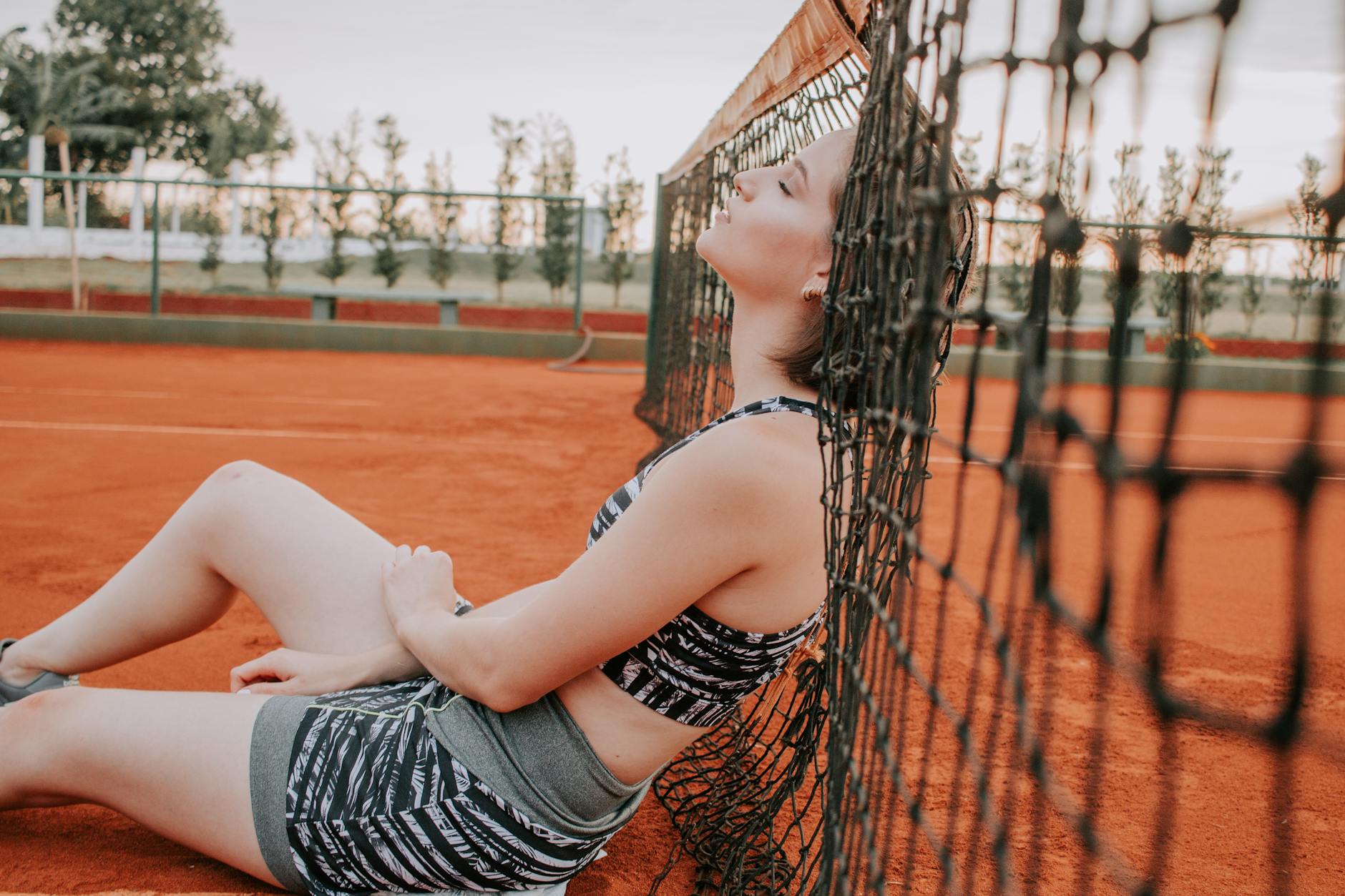 Woman resting against a tennis net on a clay court in Medianeira, Brazil.