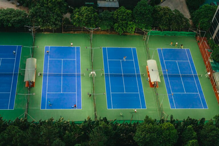 Tennis courts from above showcasing players in action, surrounded by greenery.