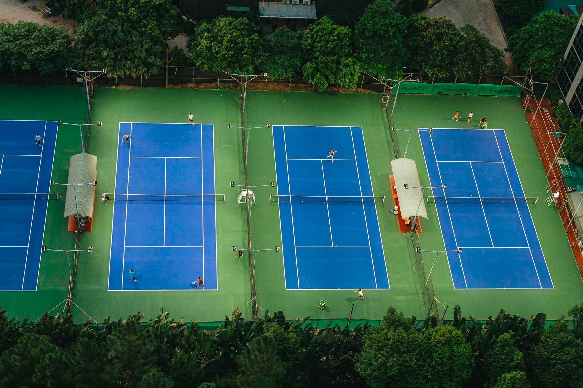 Tennis courts from above showcasing players in action, surrounded by greenery.