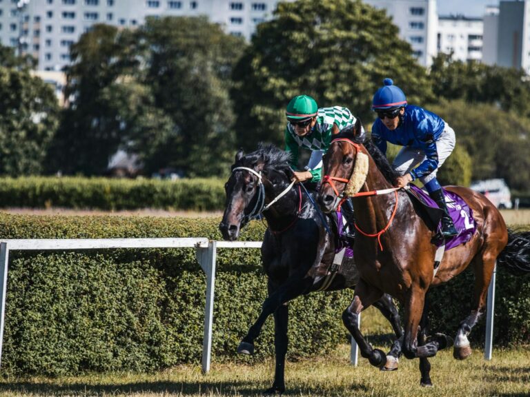 Two jockeys race fiercely in a horse racing event on a sunny day.