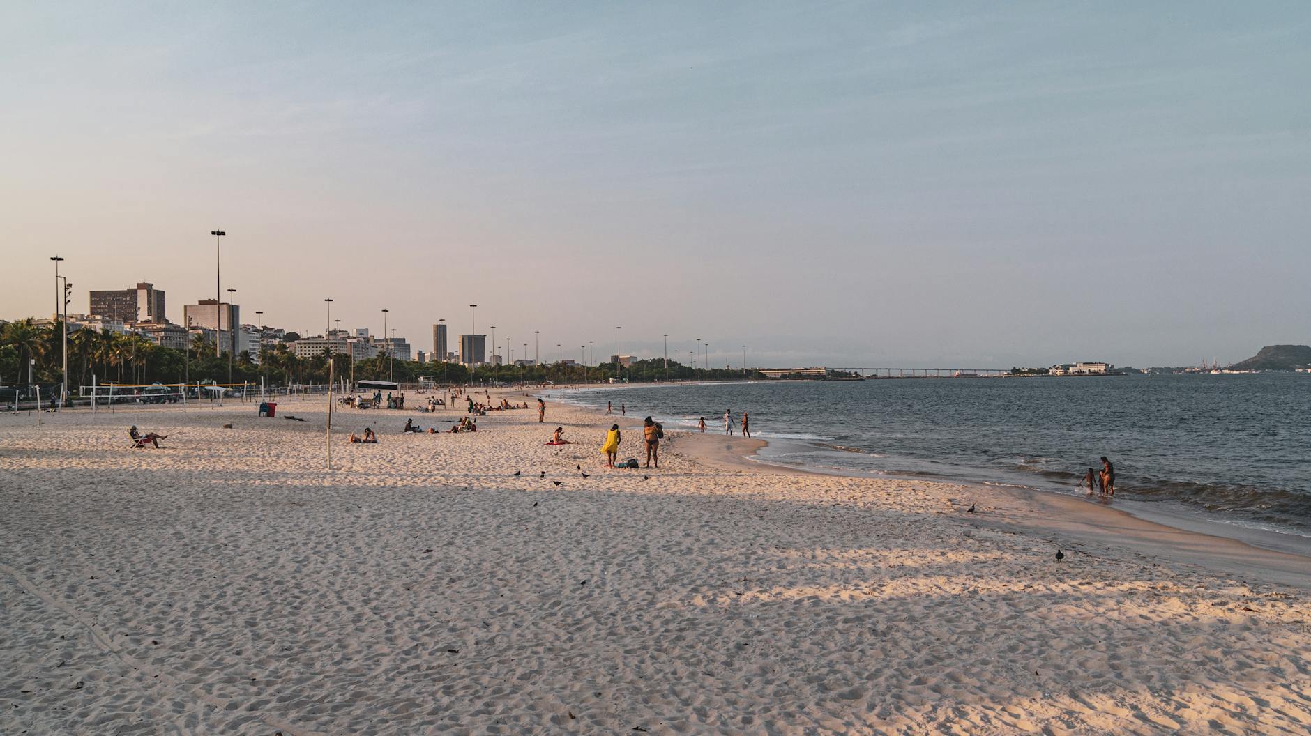 People enjoying a sunny day on Flamengo Beach in Rio de Janeiro, with city skyline views.