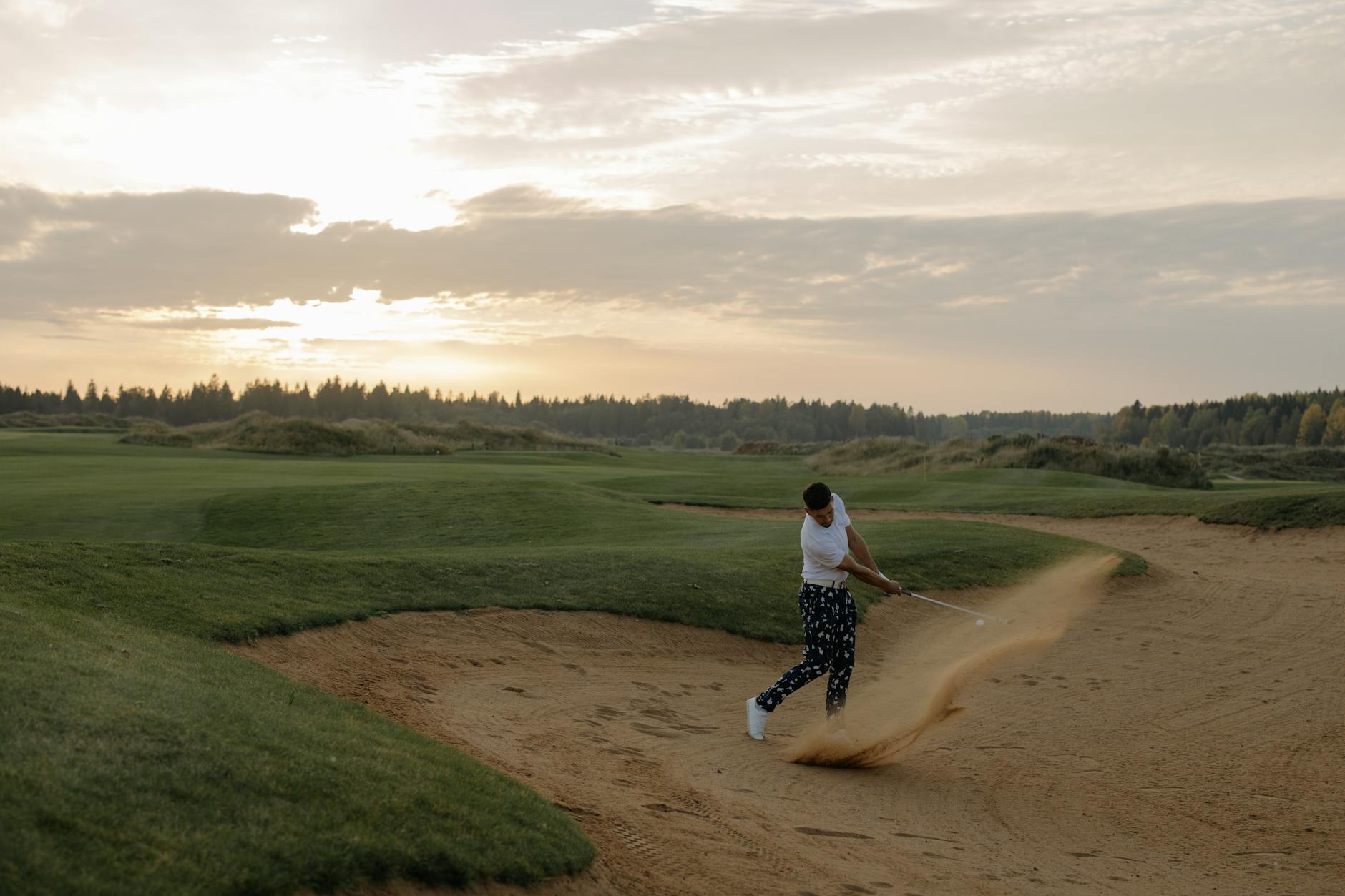 Golfer hitting a sand shot at sunset on a scenic golf course, showcasing skill and landscape.