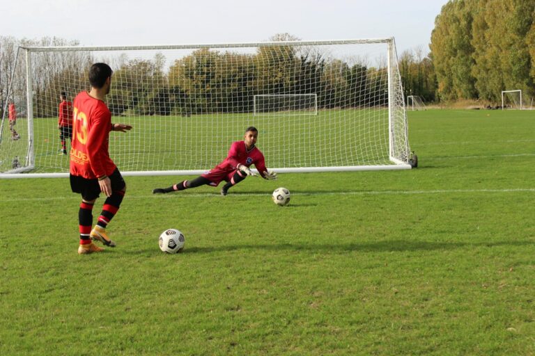 A soccer player prepares to take a shot as the goalkeeper dives to save in an outdoor match.