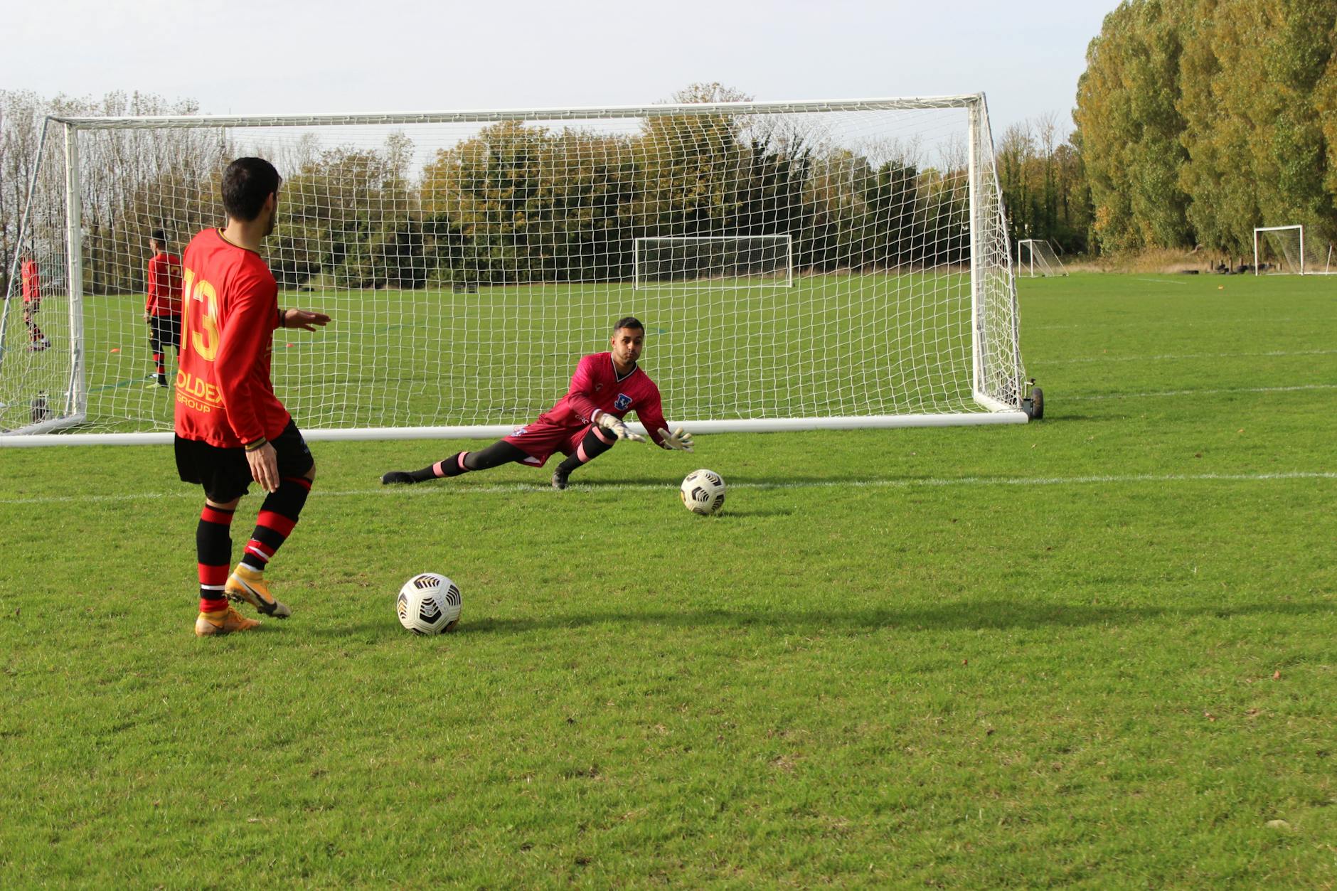 A soccer player prepares to take a shot as the goalkeeper dives to save in an outdoor match.