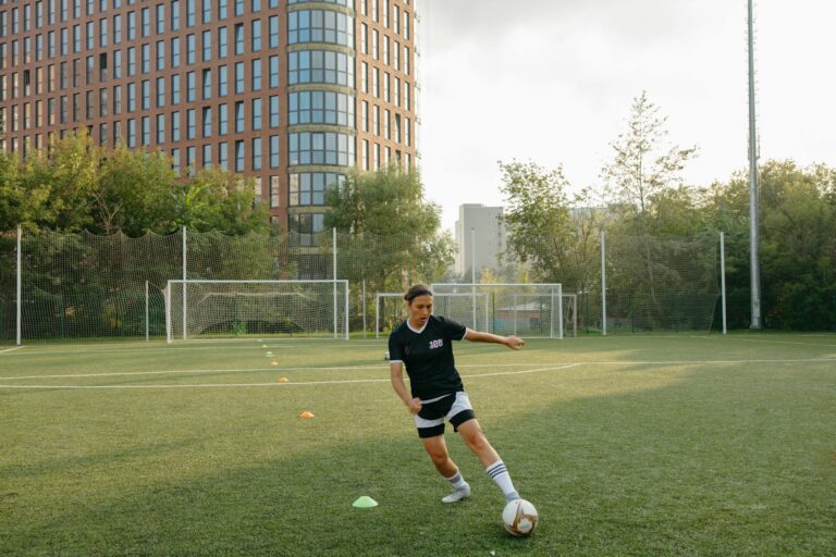 A woman practicing soccer skills on a city field with tall buildings in the background.