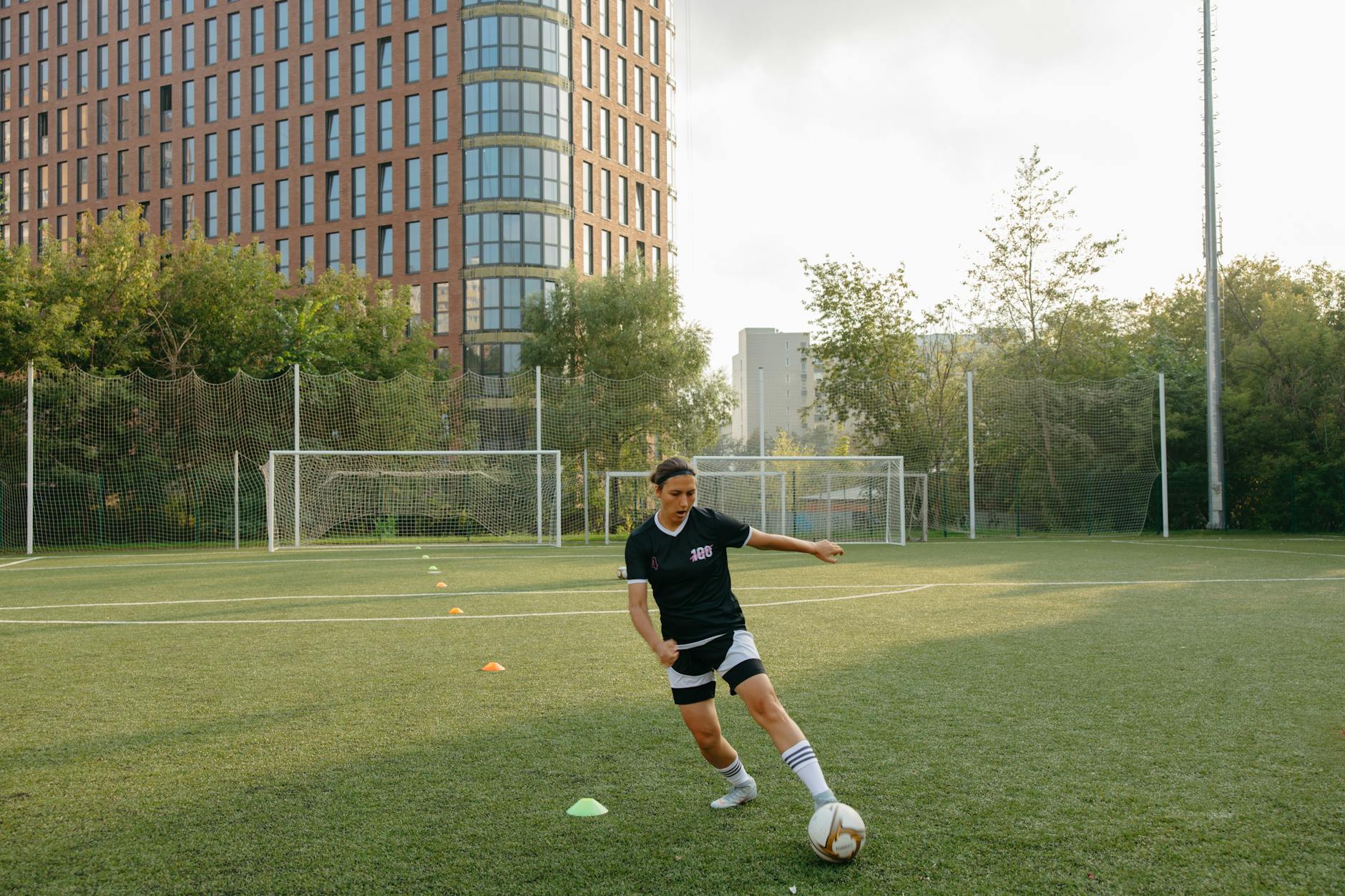 A woman practicing soccer skills on a city field with tall buildings in the background.