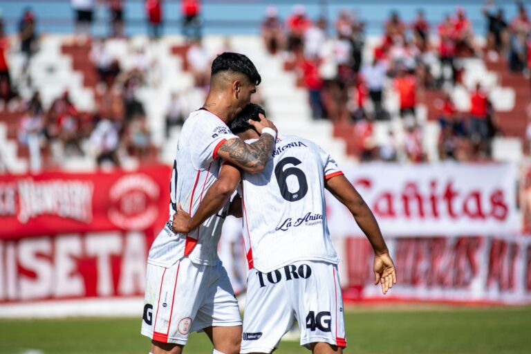 Two soccer players celebrating a goal with a crowd in the background.