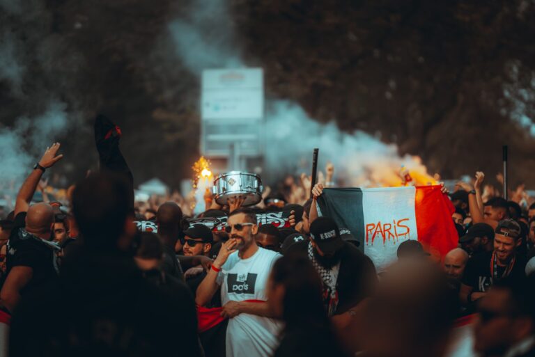 A lively crowd of football fans celebrating with smoke flares and flags in Paris streets.