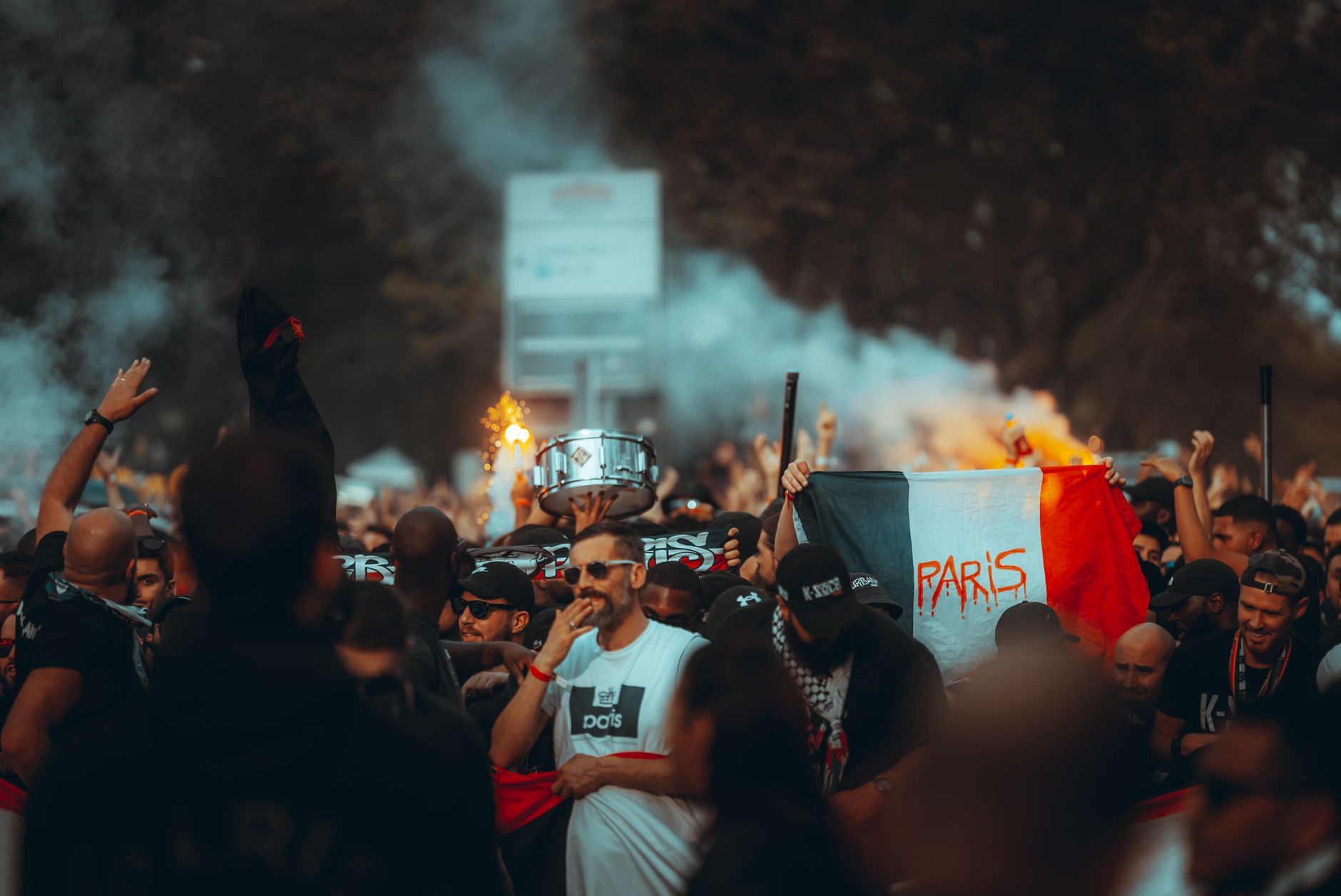 A lively crowd of football fans celebrating with smoke flares and flags in Paris streets.