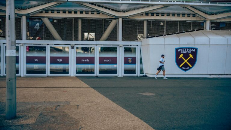 A person walking by West Ham United football stadium entrance in London.