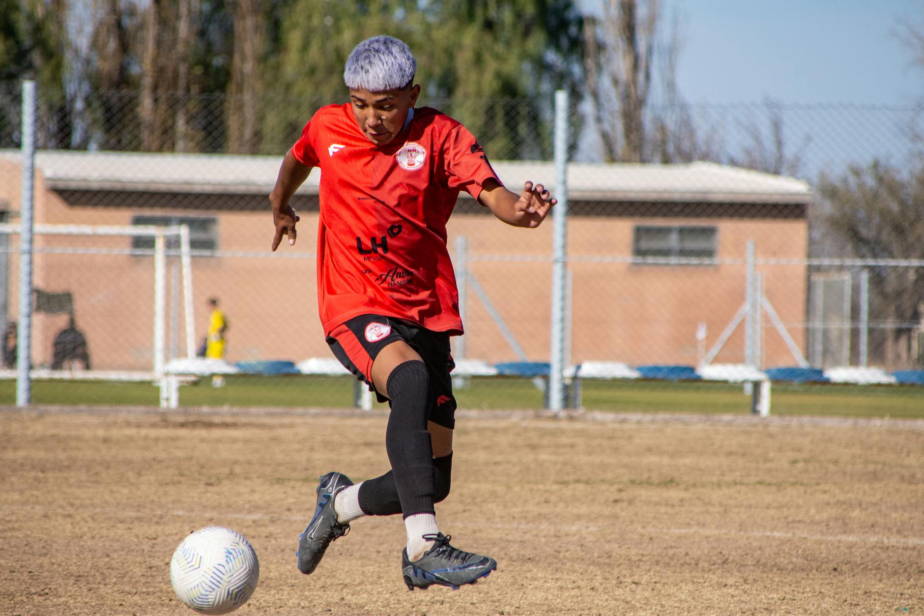 Young male soccer player skillfully dribbles the ball on a sunny day at an outdoor field.