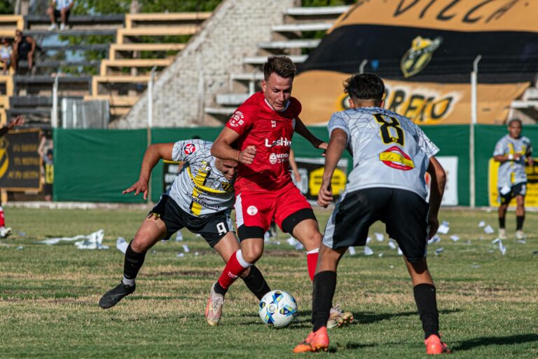 Three male soccer players competing intensely on a grassy field.