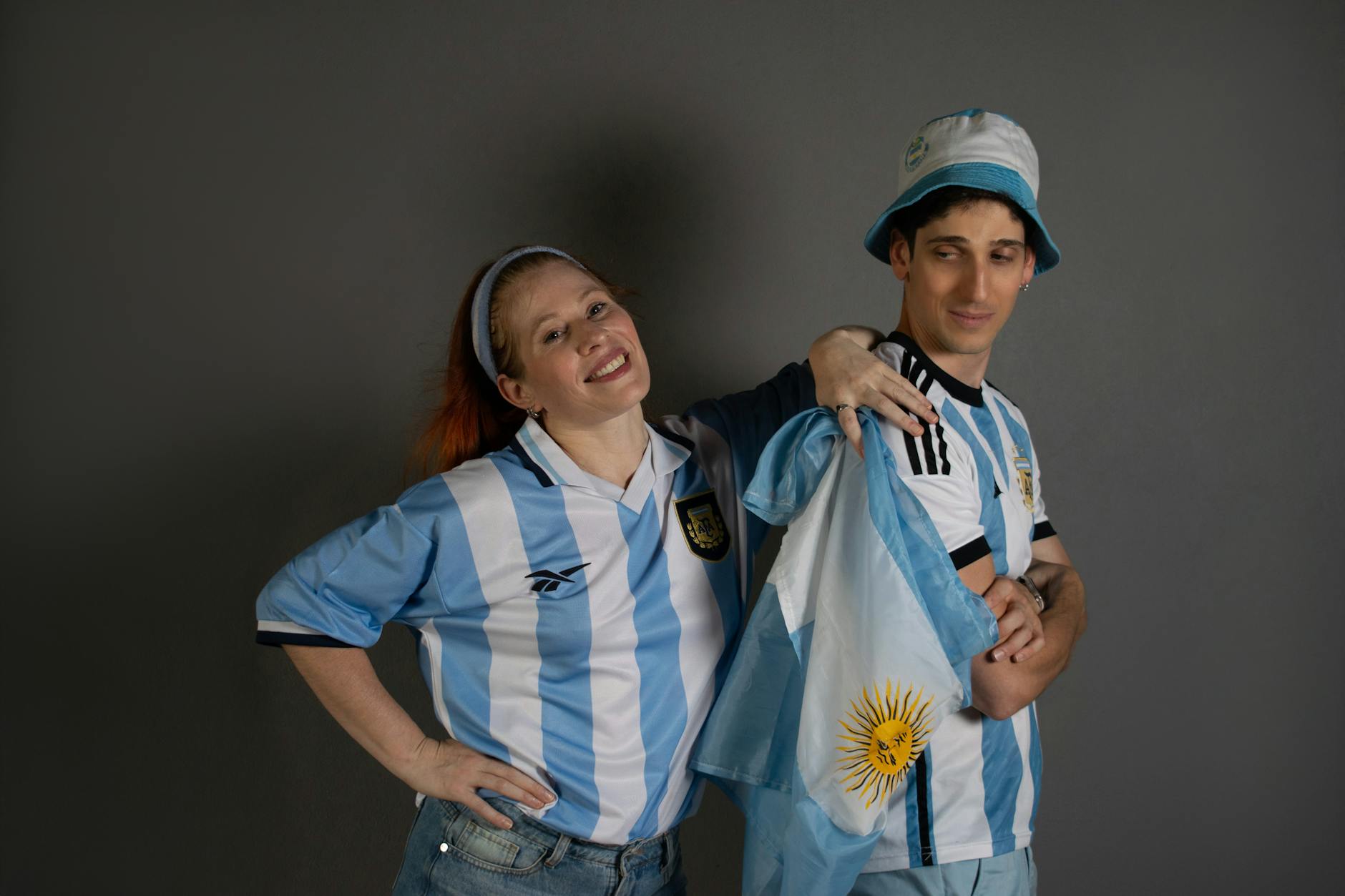 Two joyful Argentina soccer fans in team jerseys with a national flag, celebrating enthusiastically.