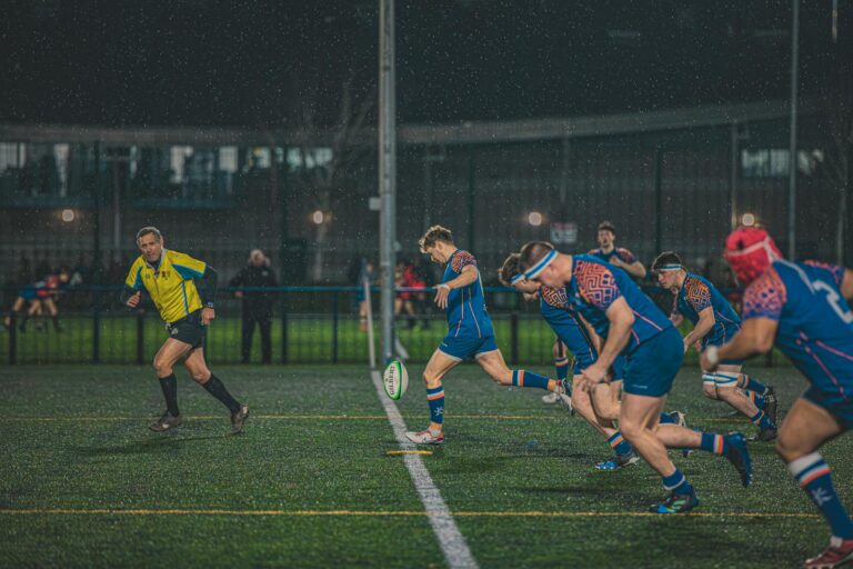 Intense night-time rugby match in England, capturing action and teamwork on a rainy field.