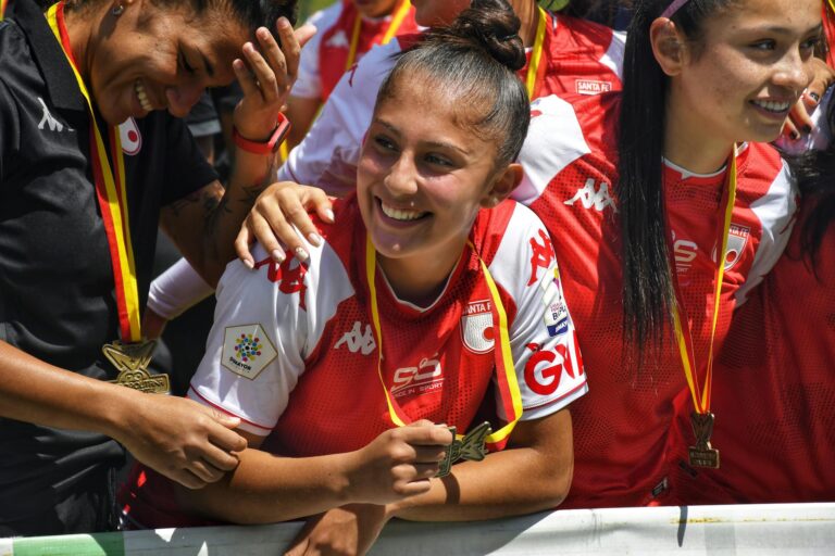 Smiling women football players celebrate with medals after victory. Sunny outdoor team moment.