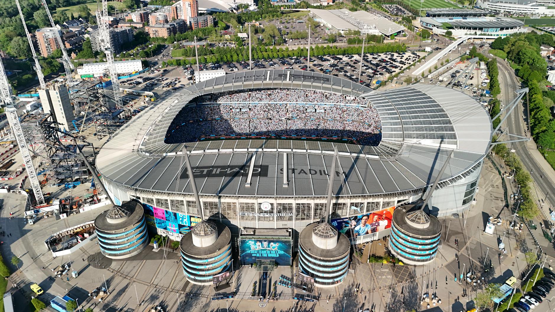 Drone shot of a packed Etihad Stadium in Manchester, England, showcasing a vibrant cityscape.