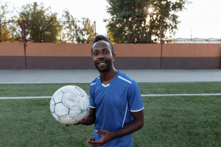 A joyful soccer player in a blue jersey holds a soccer ball on a grass field, ready to play.