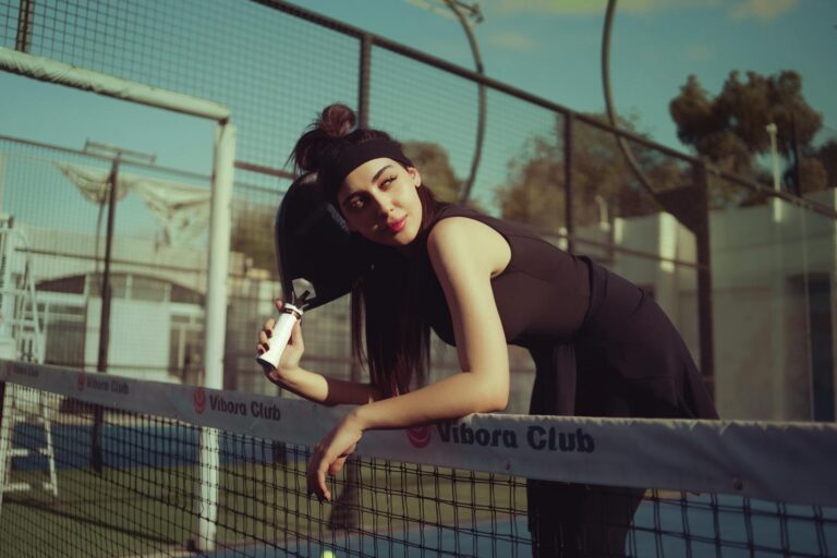 A young woman leaning on a tennis net outdoors on a sunny day in Baghdad, Iraq.