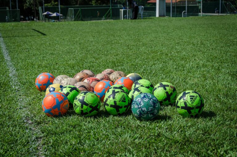 A collection of colorful soccer balls on a green field in Brasília, Brazil, under a clear blue sky.