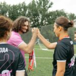 Soccer team celebrating victory on field with coach, exchanging fist bumps and medals.