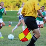Women's soccer match featuring players and referee on field in motion.