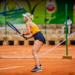 Blonde woman playing tennis on a clay court, focused and ready for action.