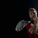 A thoughtful male tennis player holding a racket, set against a dark background.