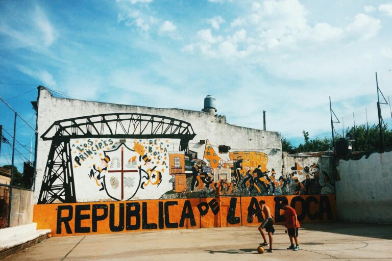 Two kids play soccer against a vibrant urban mural in San Nicolas, Buenos Aires.