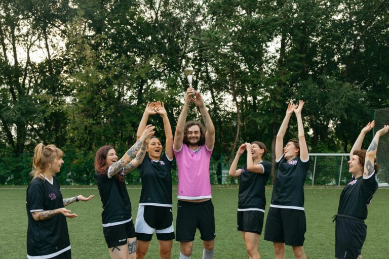 A joyful soccer team celebrates victory with a trophy on a green field.