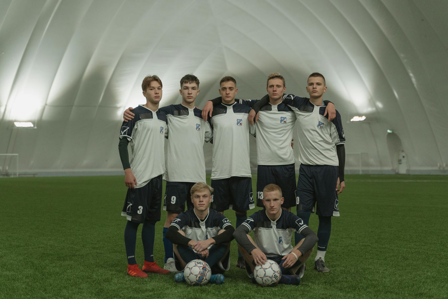 A group of young male soccer players in uniform posing on an indoor field.