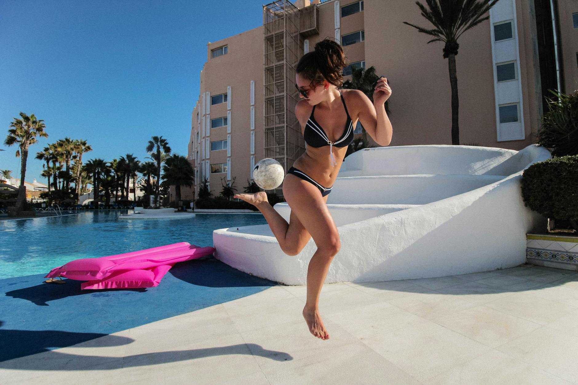 A woman skillfully kicks a soccer ball by the pool at a sunny resort in Almería, Spain.