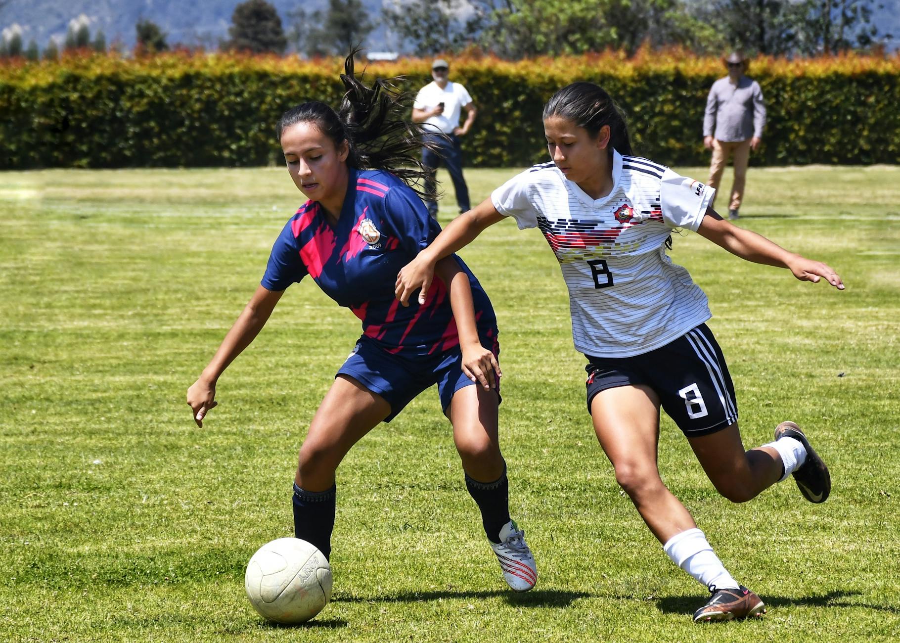 Two female soccer players competing fiercely on a sunny day outdoors.