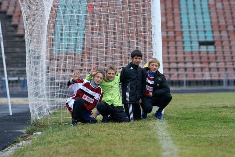 Four young soccer players posing by a goal on a stadium field.