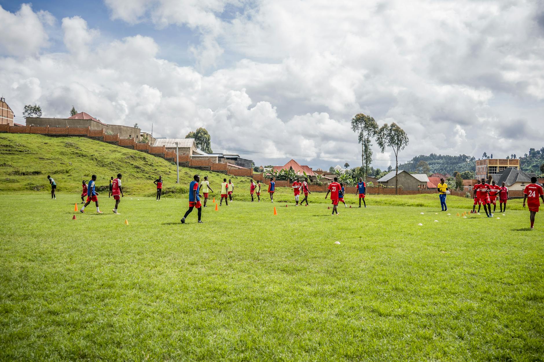 Teenagers playing football on a grassy field with houses and mountains in the background.