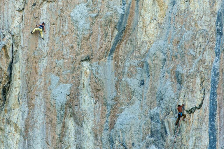 Two rock climbers tackle a steep, textured cliff face, showcasing their skill and determination.