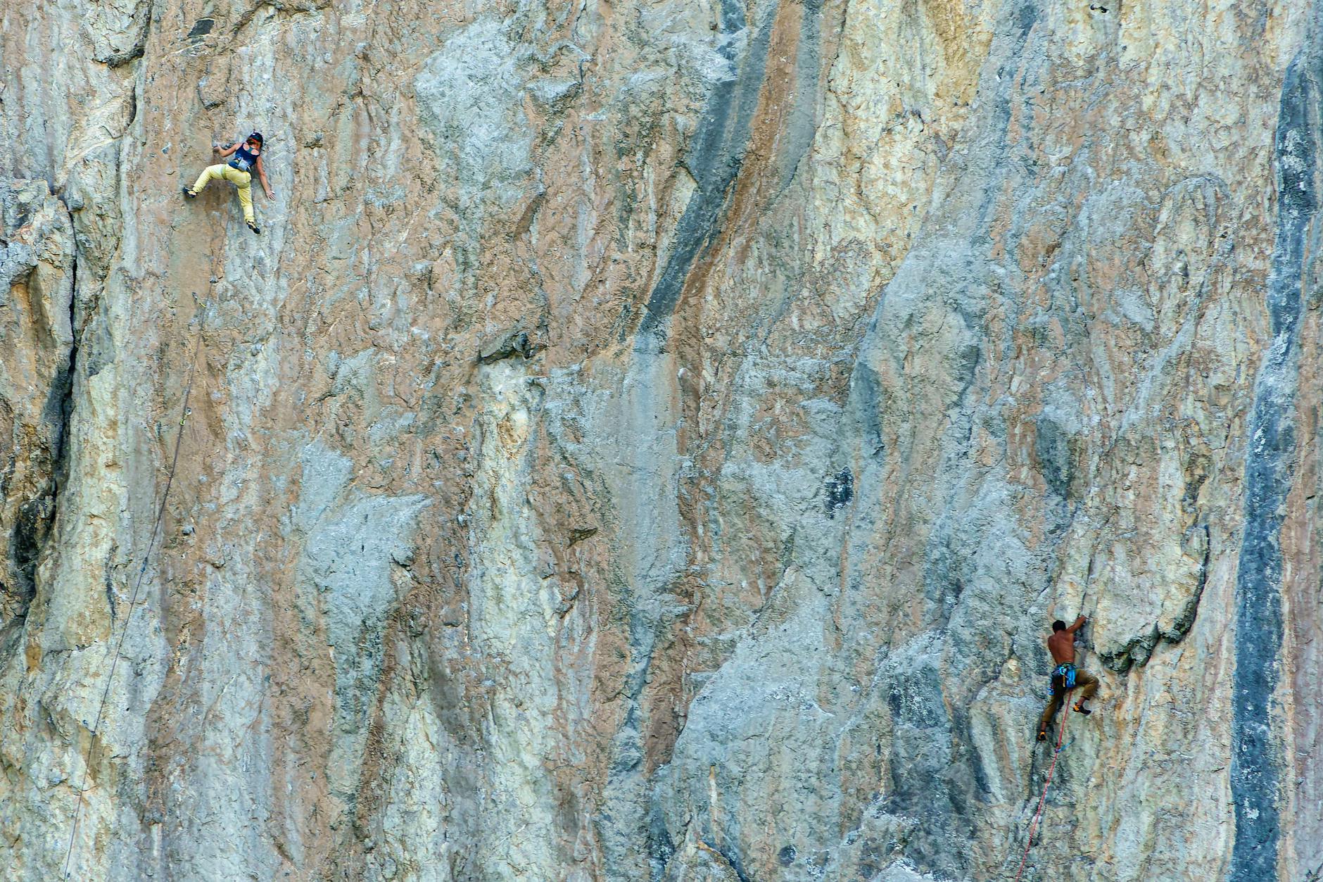 Two rock climbers tackle a steep, textured cliff face, showcasing their skill and determination.