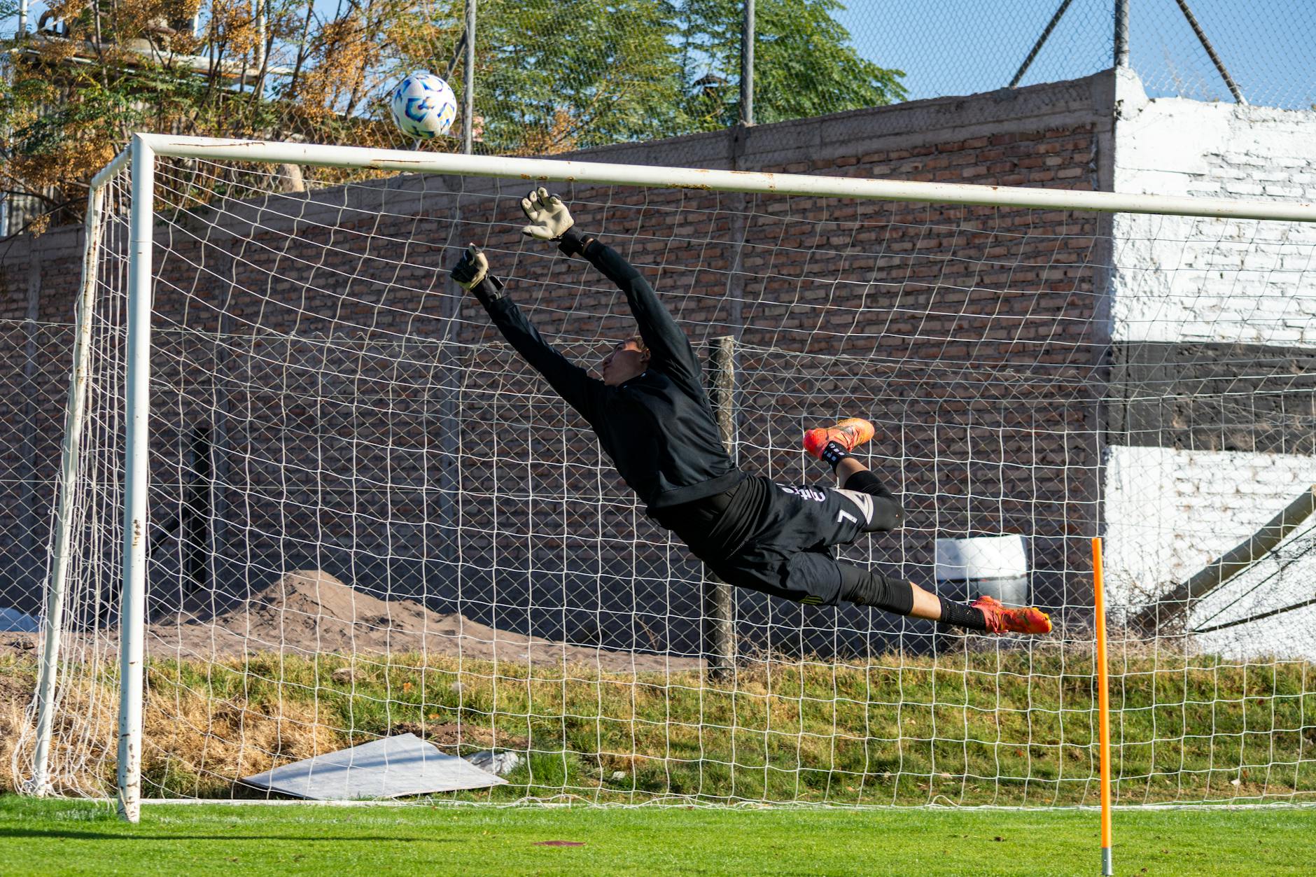 Dynamic action shot of a goalkeeper making a high save during a soccer game outdoors.