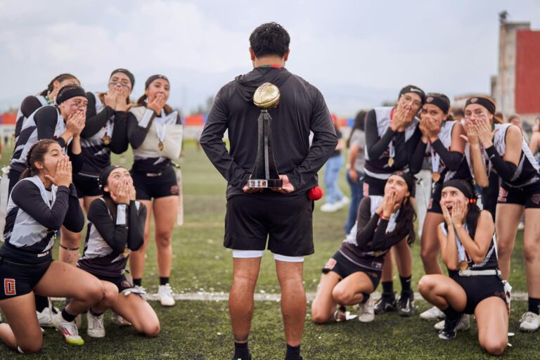 Excited female team celebrating a sports victory with their coach holding a trophy.
