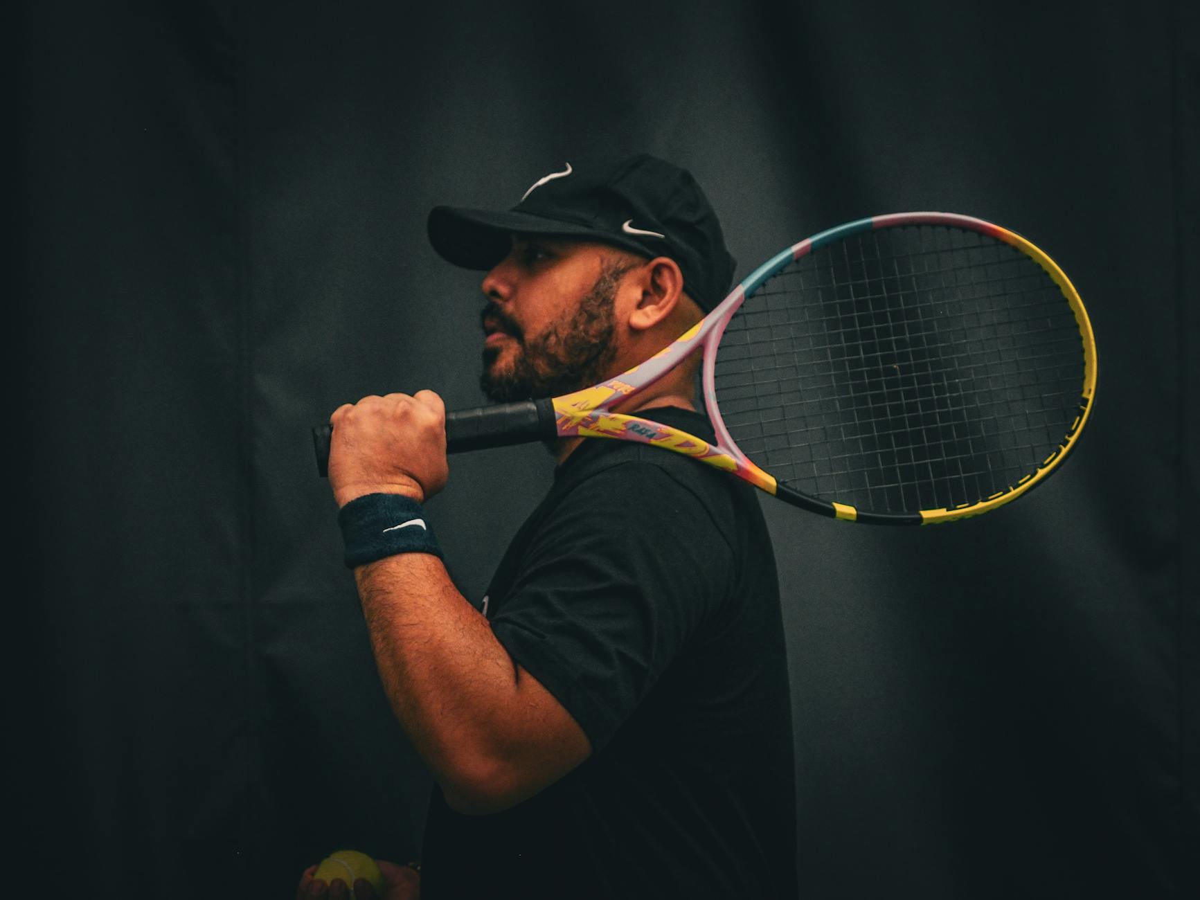 Portrait of a focused male tennis player holding a racket against a dark background.