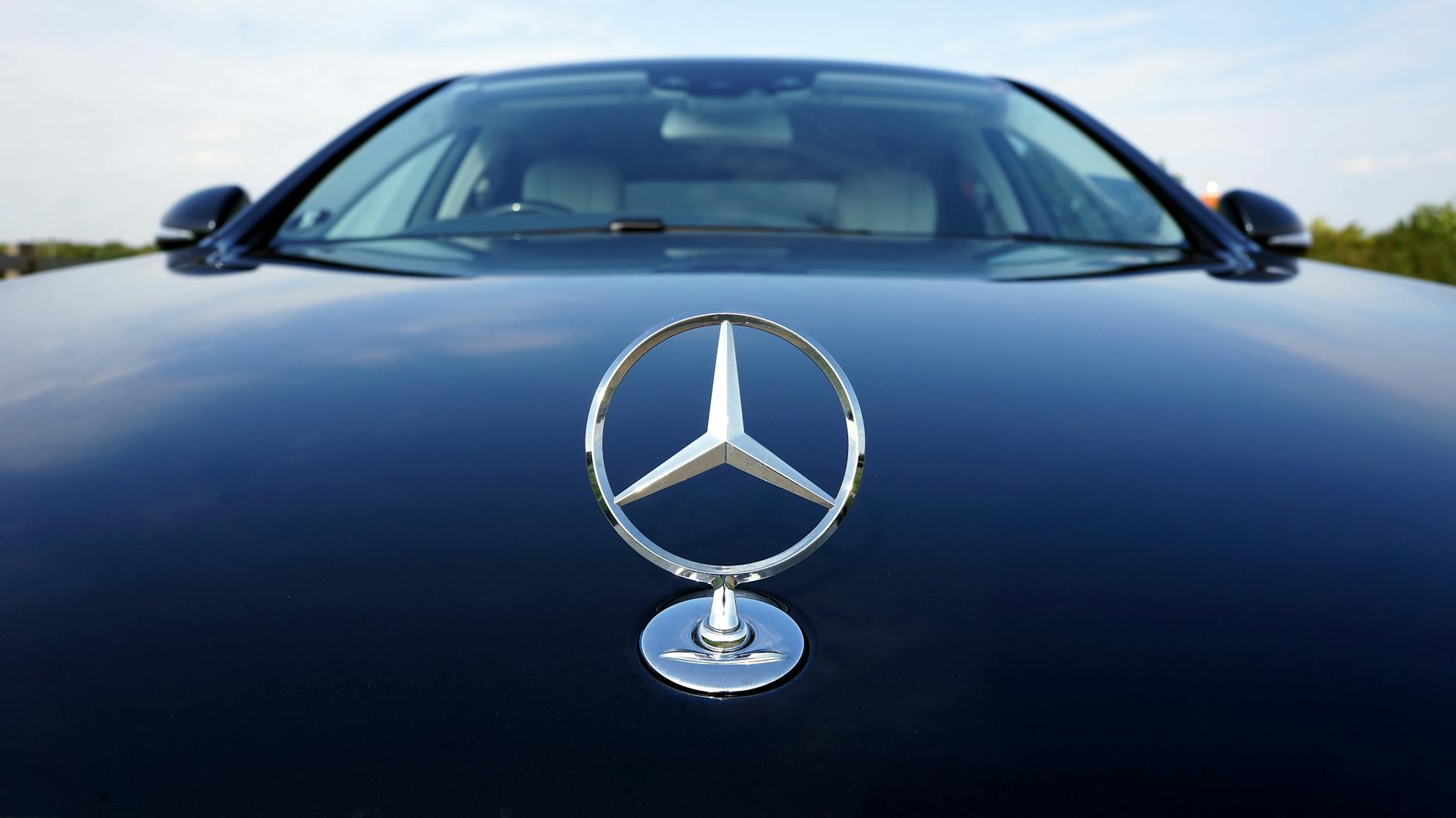 Close-up of a Mercedes-Benz emblem on a luxury car hood featuring a sleek design.